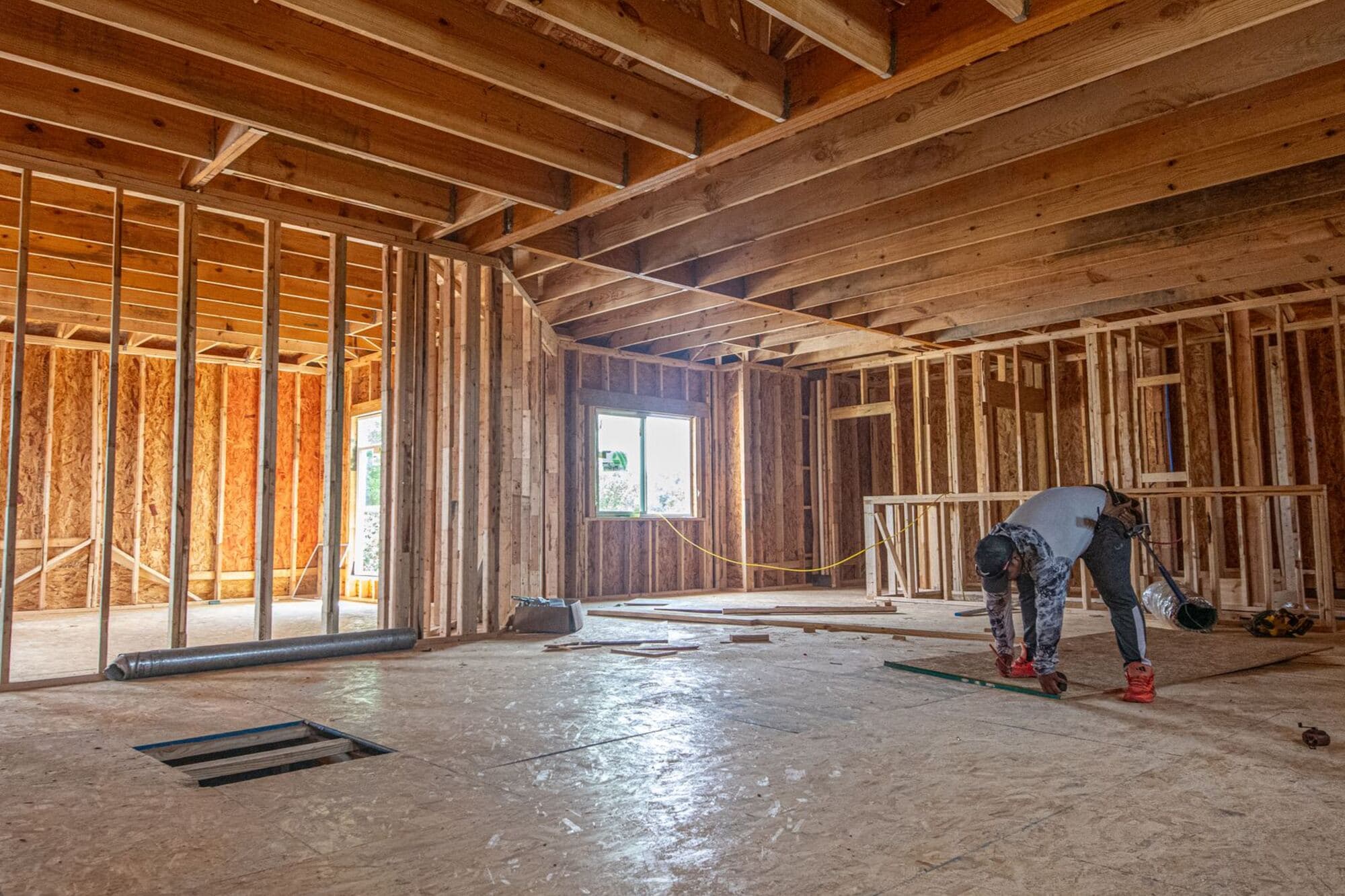 Interior framing of a house under construction, with a worker at the far end